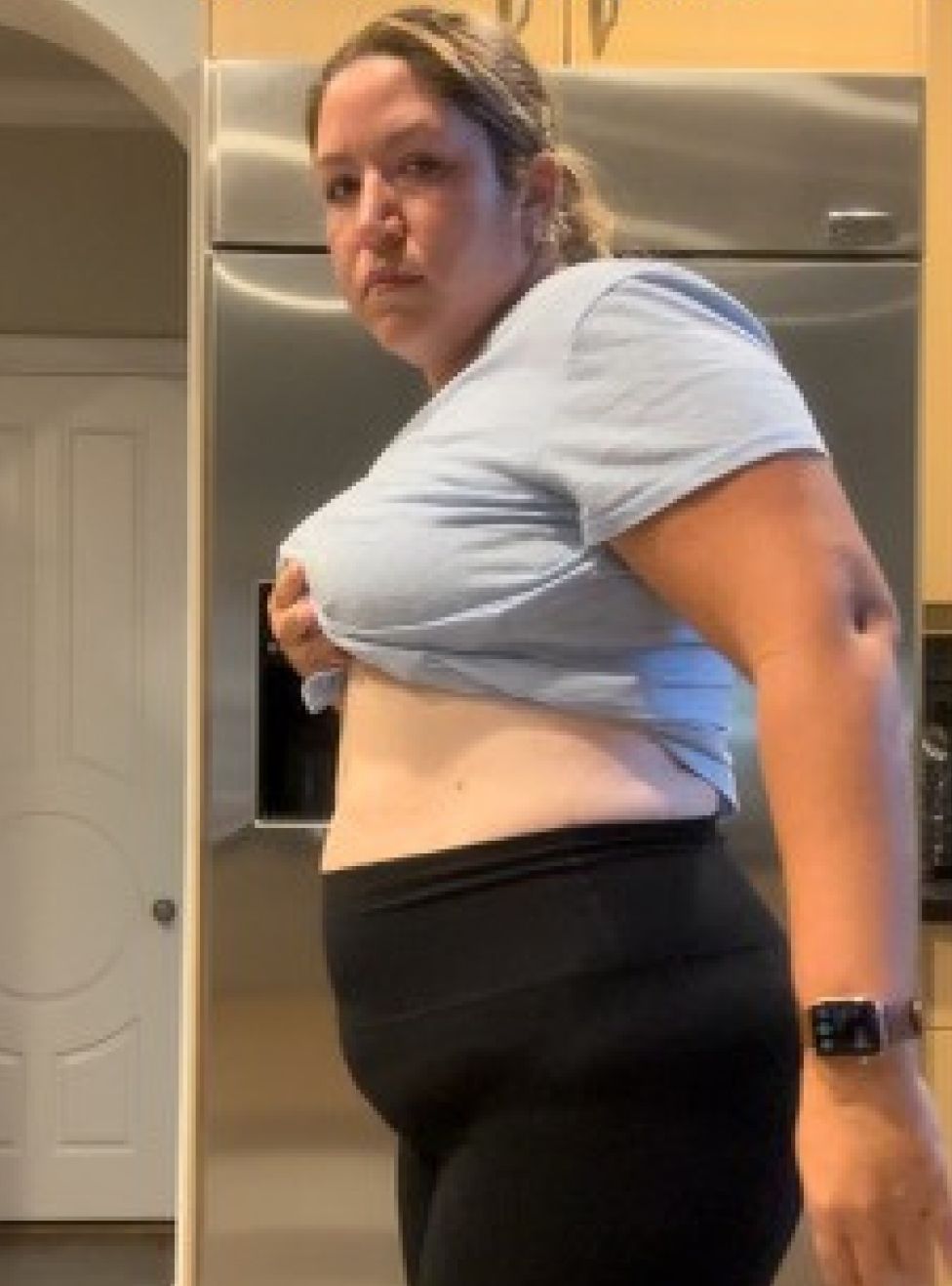 A woman in a blue shirt and black pants is standing in front of a refrigerator