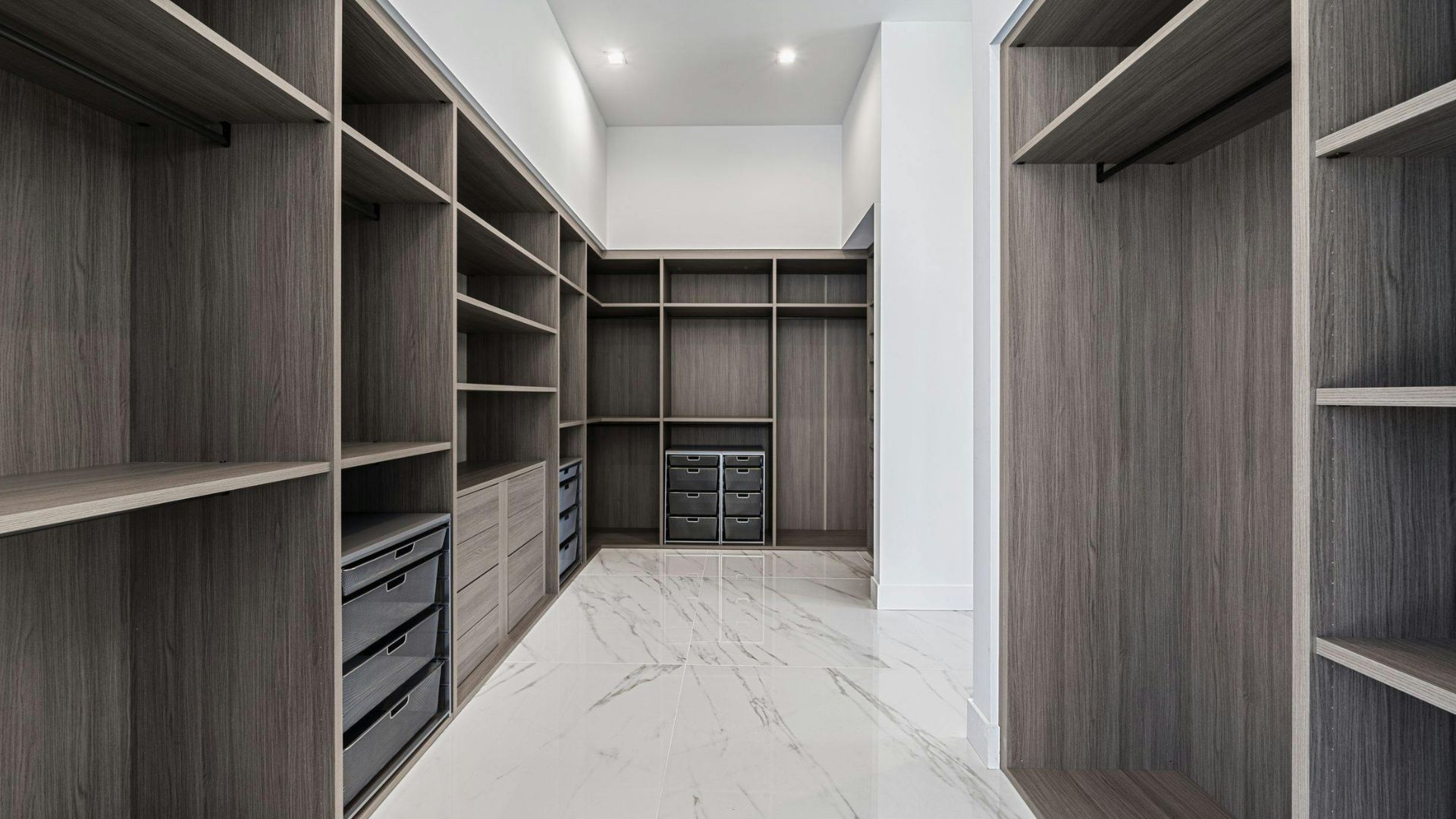 Modern walk-in closet with gray wood shelving, drawers, and white marble floor.