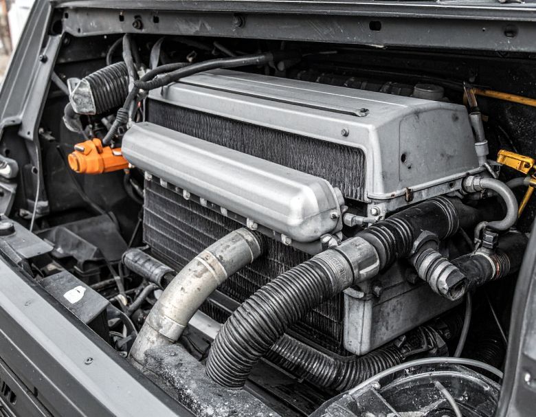 Engine of a vehicle, with a large, rectangular metallic block and various hoses.