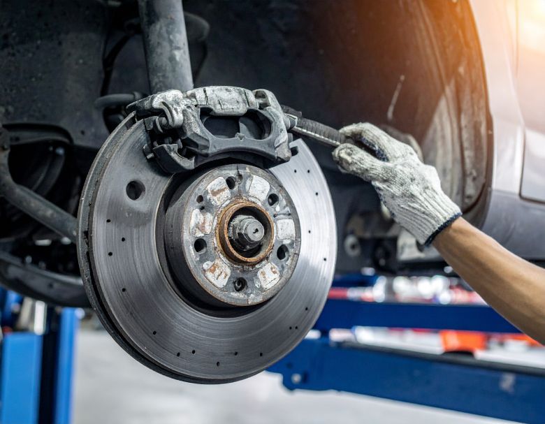 Mechanic working on car's brake rotor; holding wrench, wearing glove. Close-up shot, blue lift, garage setting.