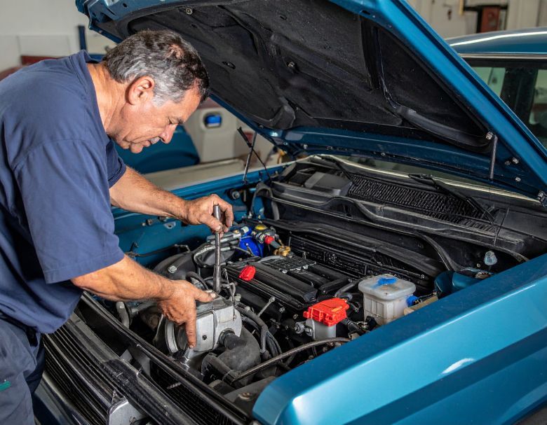 Mechanic working on a blue car engine with hood open, using a wrench.