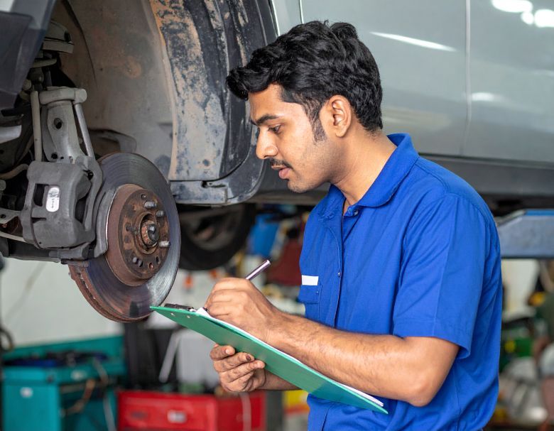 Mechanic inspecting car brakes, writing on a clipboard in a garage.
