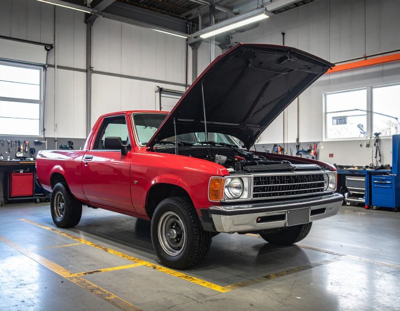 Red pickup truck with hood open in a garage.
