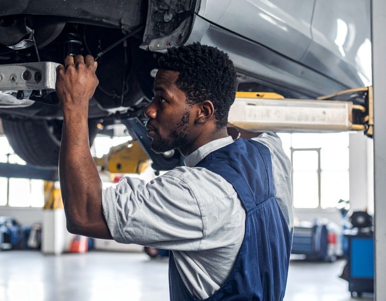 Mechanic working under a car lifted on a hoist in a garage.