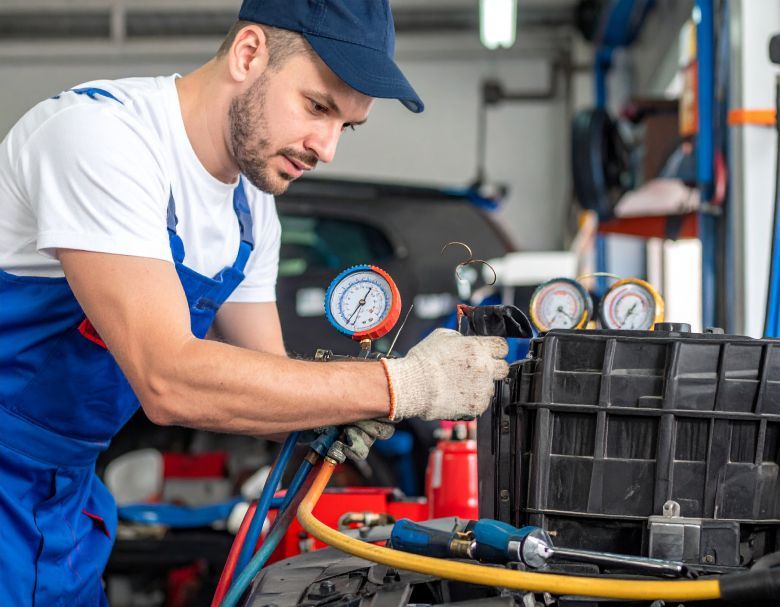 Mechanic in blue overalls checking car's engine with gauges in a garage.