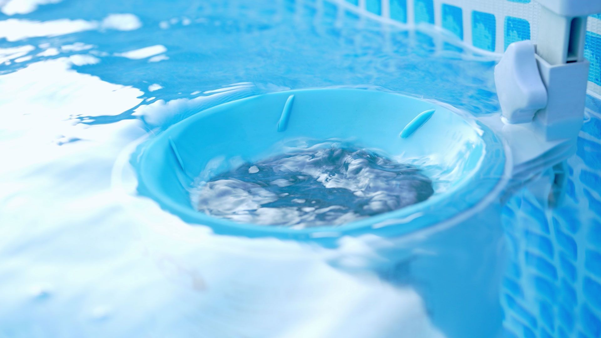 Blue pool water surrounds a blue chlorine floater with a tablet inside, attached to a pool wall.