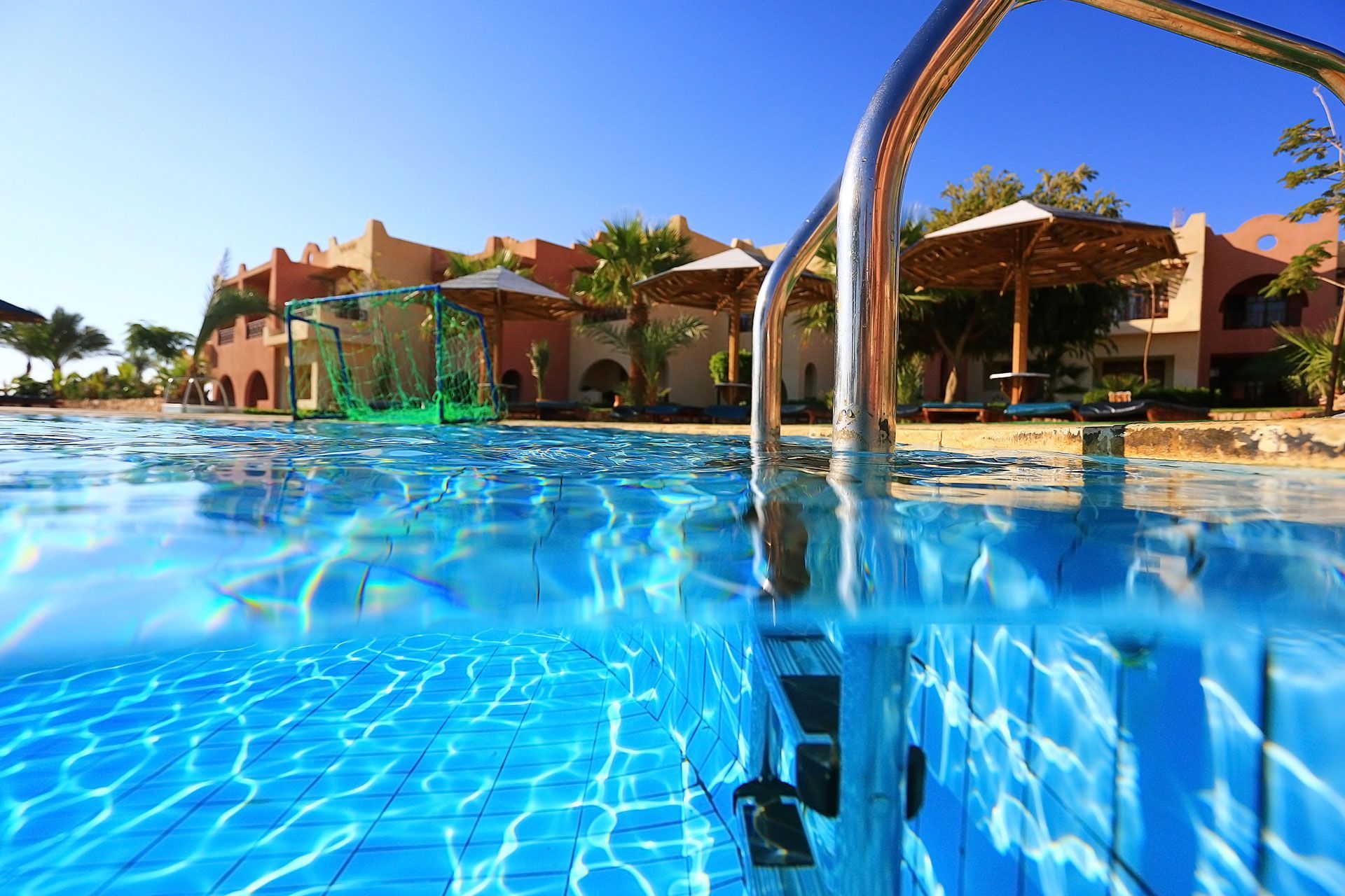 Pool with blue water and buildings in the background under a sunny, clear sky.