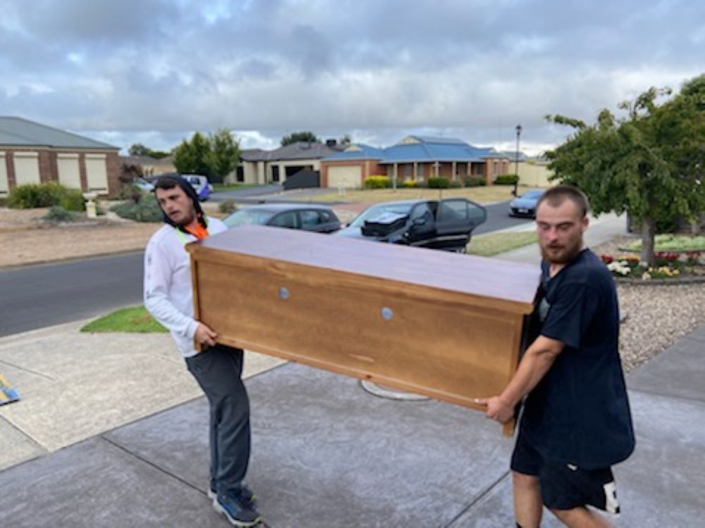 Two Men Are Carrying a Large Wooden Box on a Sidewalk — Bellarine Removals In Armstrong Creek, VIC