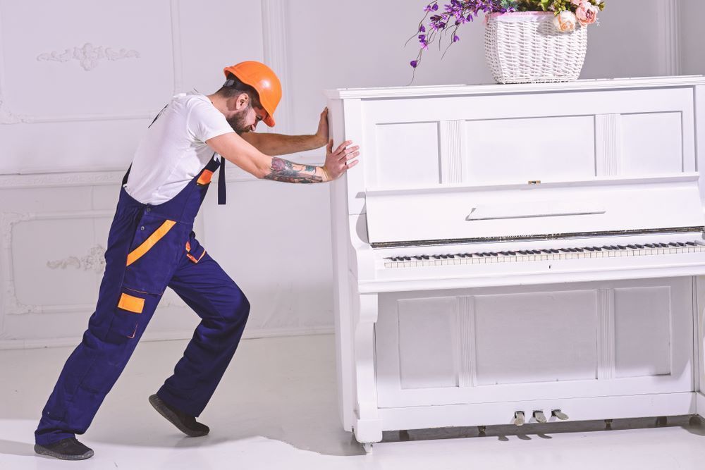 A Man is Pushing a White Piano in a Room — Bellarine Removals In Bellarine Peninsula, VIC