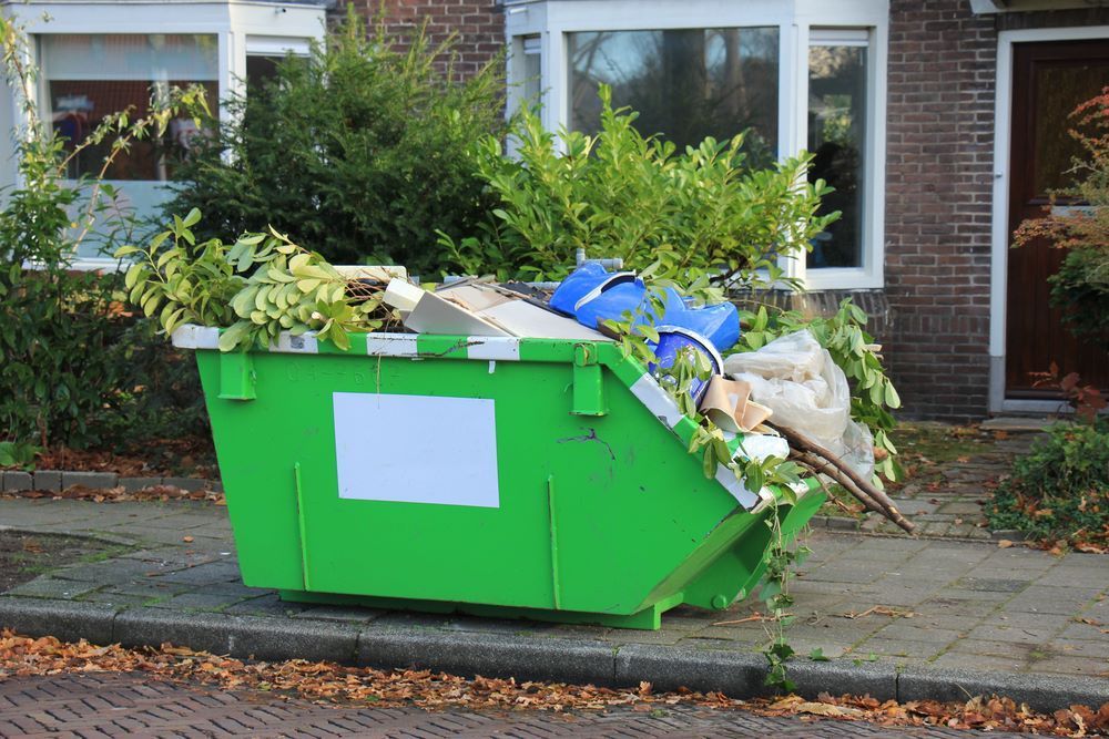 A Green Dumpster Filled With Garbage is on the Sidewalk in Front of a House — Bellarine Removals In Bendigo, VIC