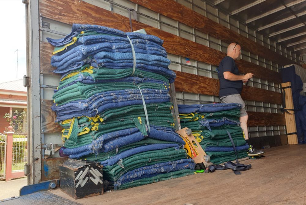 A Man is Standing Next to a Stack of Blankets in the Back of a Truck — Bellarine Removals In Colac, VIC