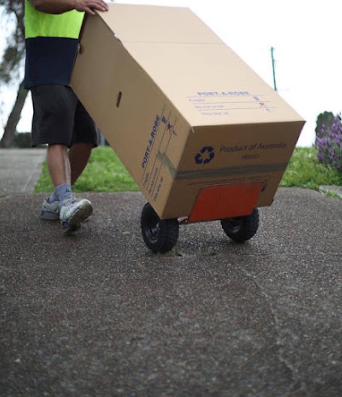 A Man is Pushing a Cardboard Box on Wheels — Bellarine Removals In Geelong, VIC