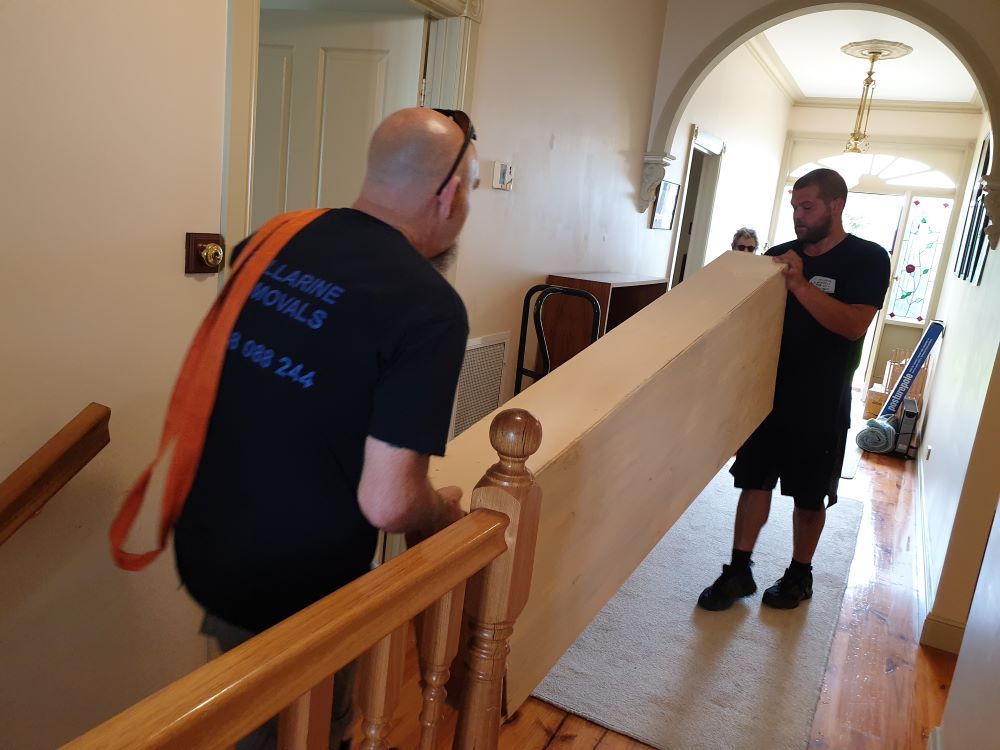 Two Men Are Carrying a Large Piece of Furniture Up a Staircase — Bellarine Removals In Ocean Grove, VIC
