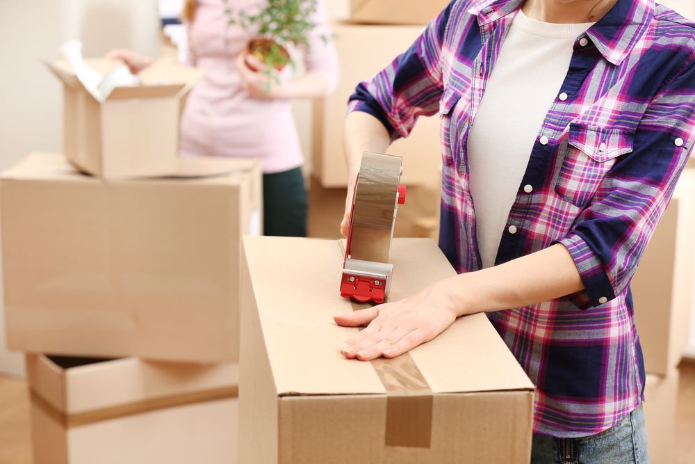 A Woman is Taping a Cardboard Box With Tape — Bellarine Removals In Geelong, VIC