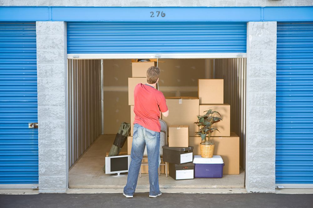 A Man in a Red Shirt is Standing in a Storage Unit Filled With Boxes — Bellarine Removals In Geelong, VIC