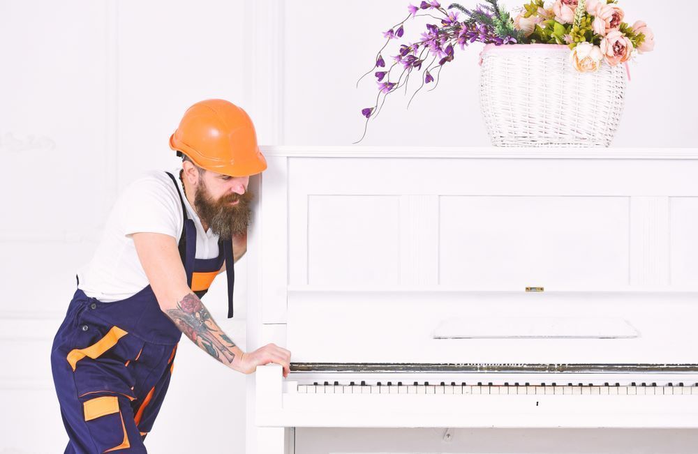 A Man Wearing a Hard Hat is Standing Next to a White Piano — Bellarine Removals In Werribee, VIC