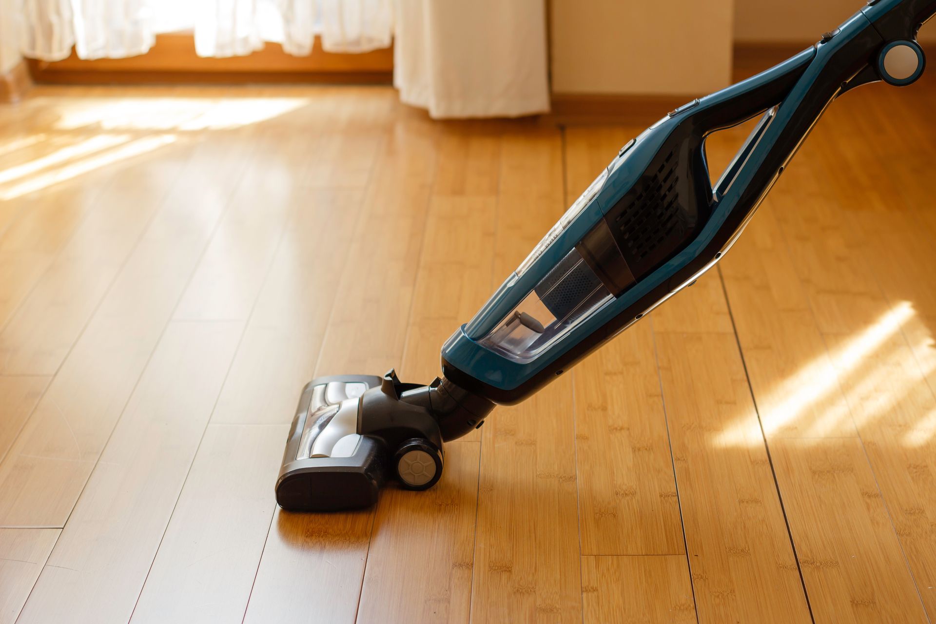 Cordless vacuum cleaning a sunlit wooden floor in a bright room. Cordless vacuum cleaning a sunlit wooden floor in a bright room.