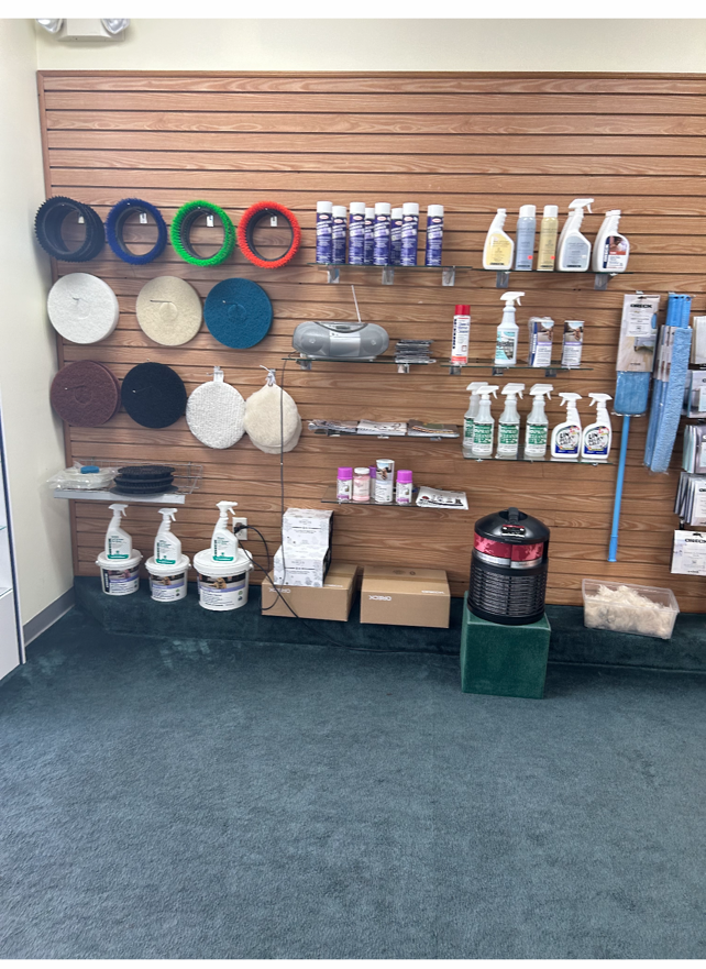 A store display showcasing cleaning supplies, including pads, bottles, and a carpet cleaner, against a wood-paneled wall.