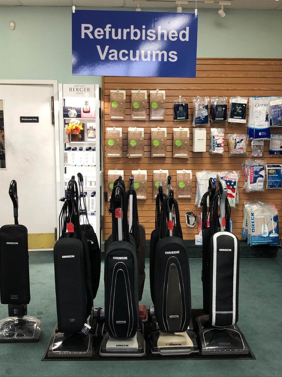 Refurbished vacuums for sale in a store, including upright models in black and white. Sign above says 