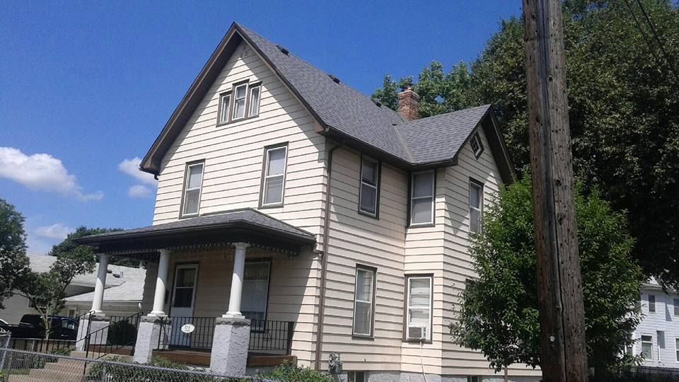 White two-story house with gray roof and front porch, seen from the street under a blue sky.