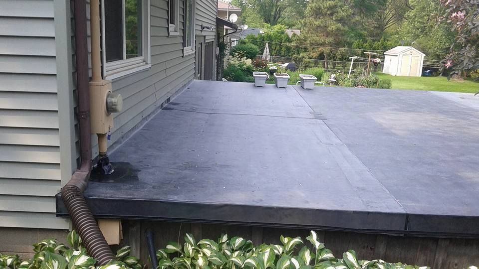 Gray flat roof beside a house, overlooking a grassy backyard with potted plants and a small shed.