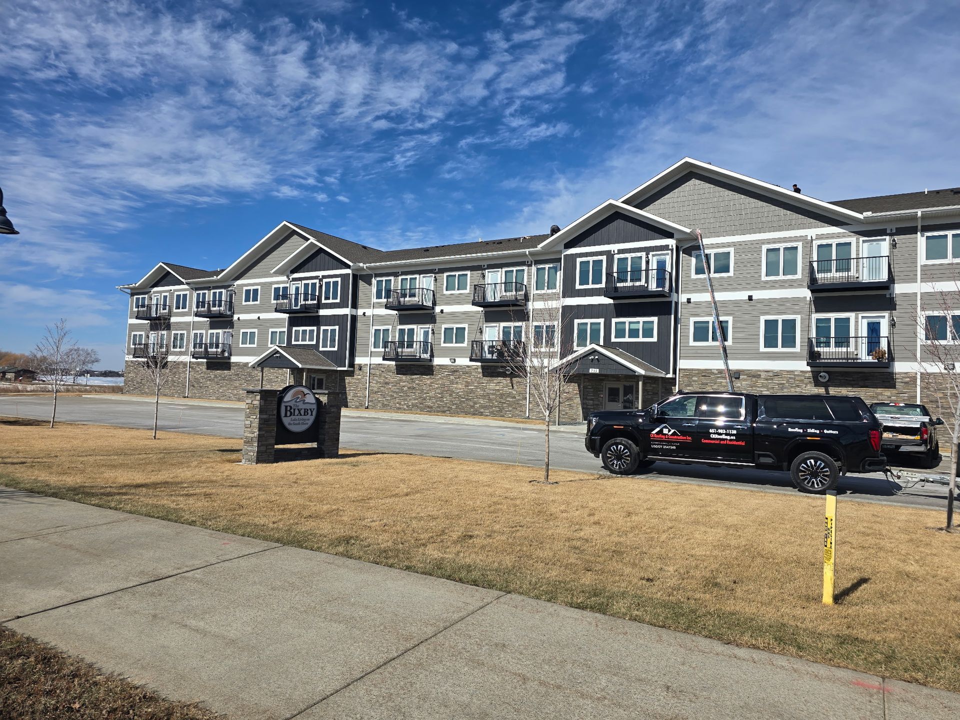 Apartment building with parked SUV beside a sidewalk under a bright blue sky