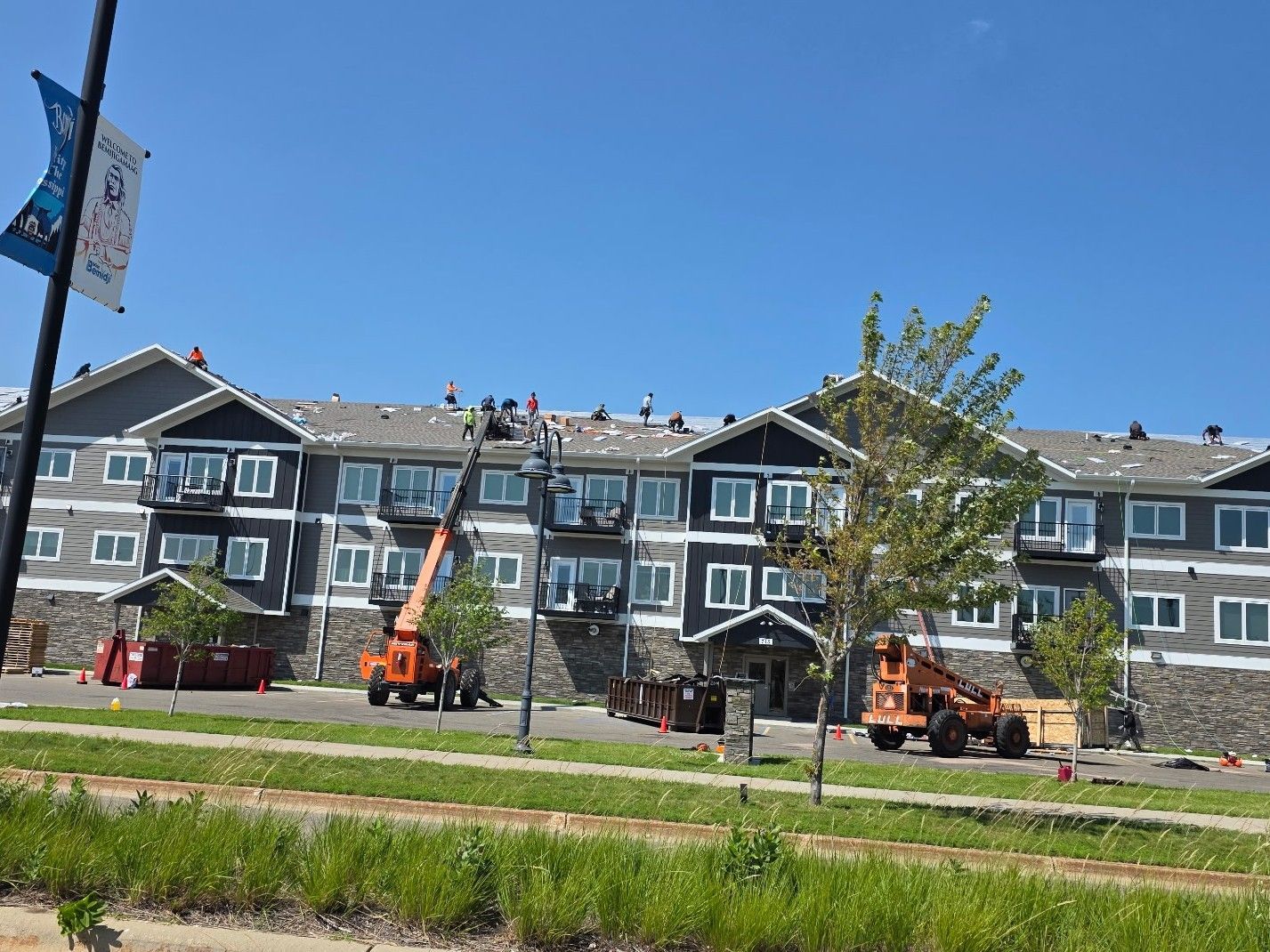 Workers and cherry picker on a townhouse roof under a clear blue sky