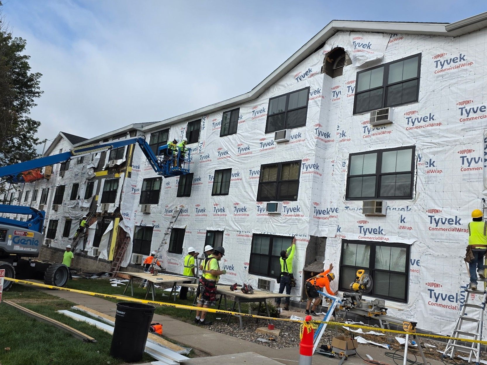 Construction workers install Tyvek wrap on a three-story building renovation site.