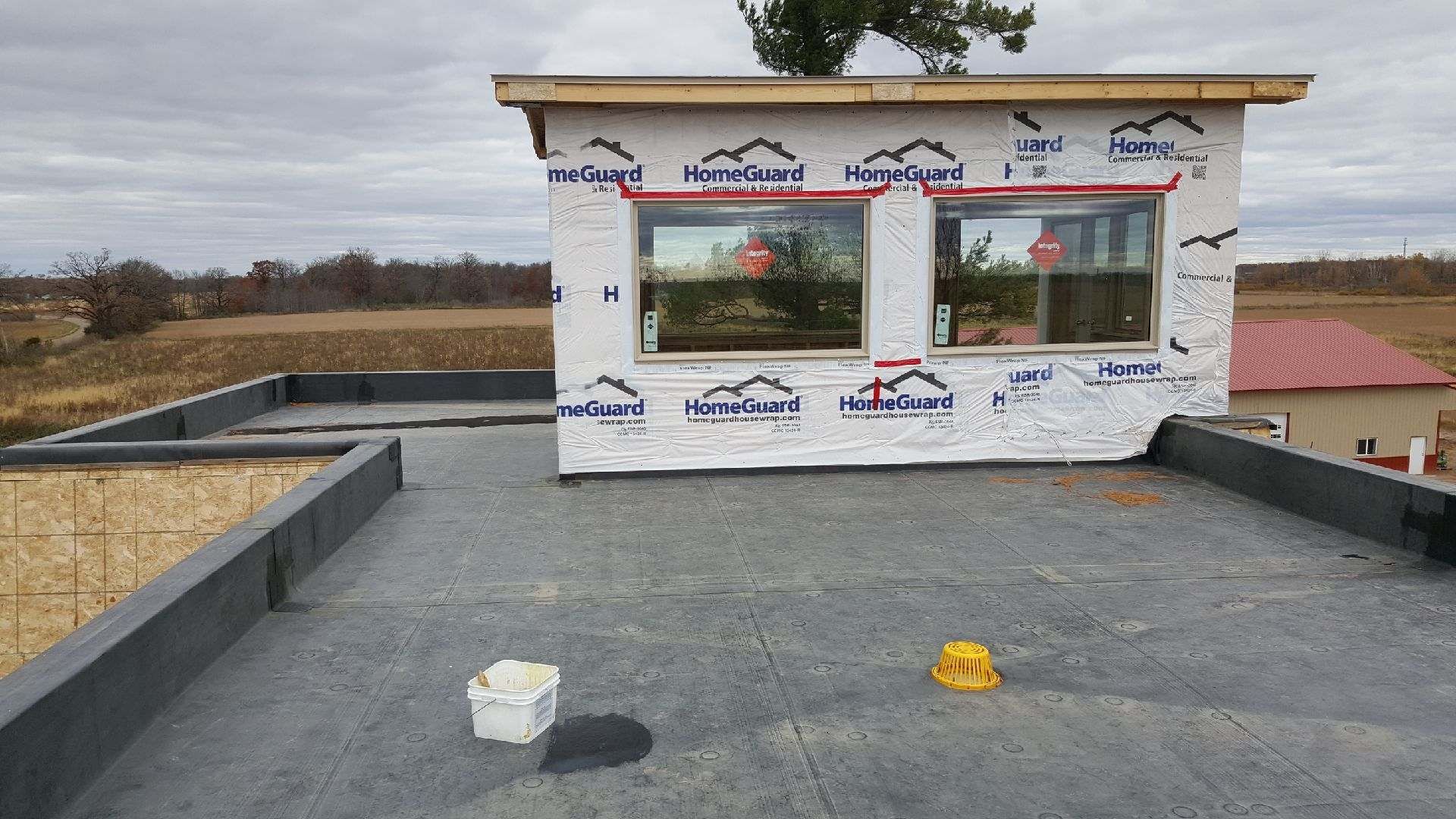 Flat rooftop with a white-framed building section, two windows, and construction materials under an overcast sky