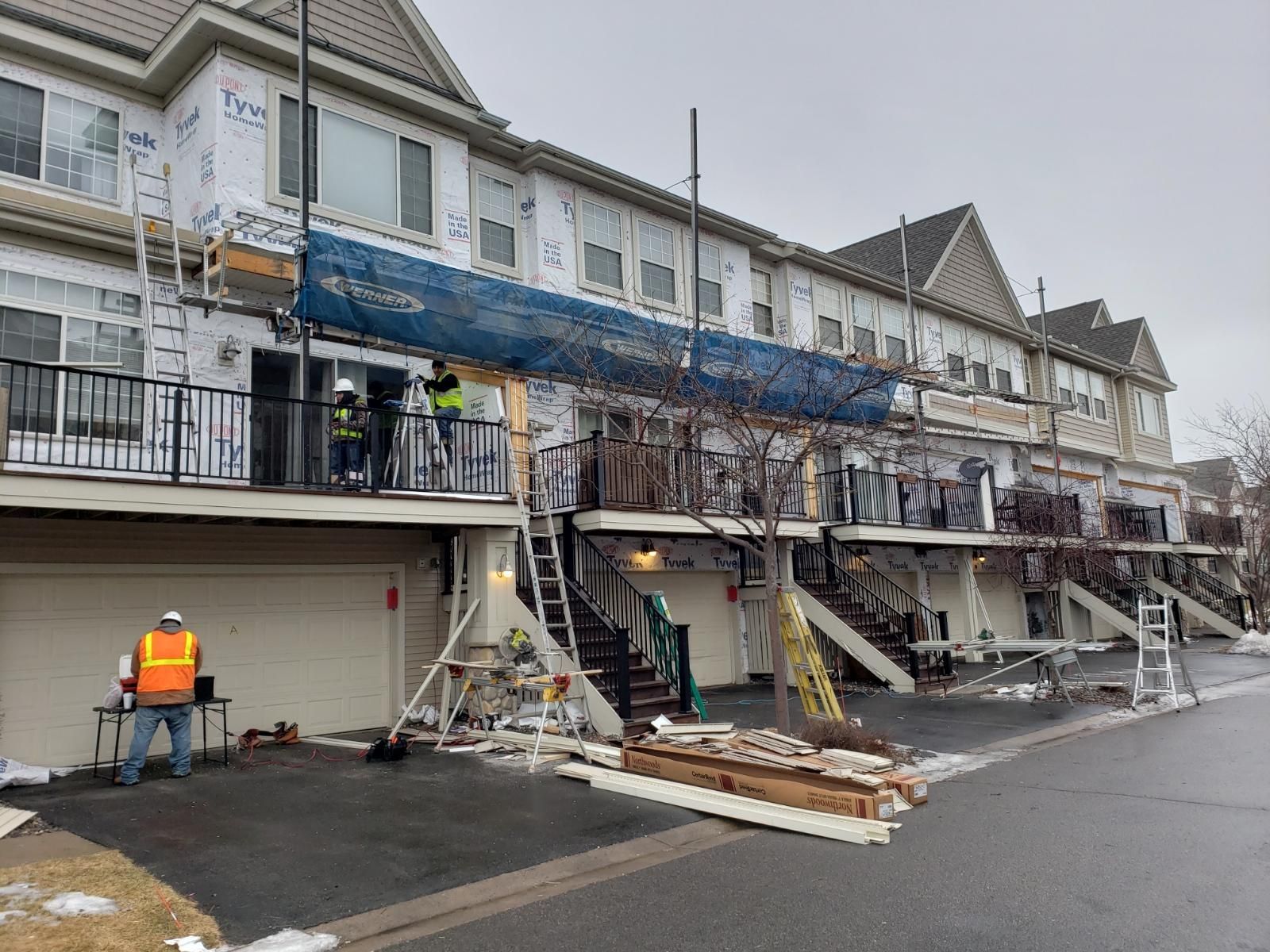 Workers repairing a damaged building facade with scaffolding, debris, and a street barricade