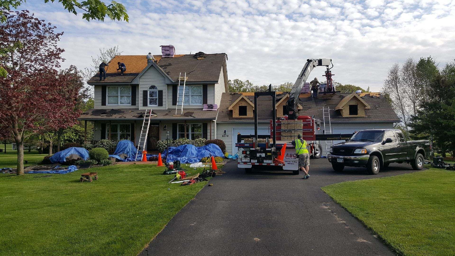 Workers and trucks in front of a house with blue tarp-covered debris after storm damage
