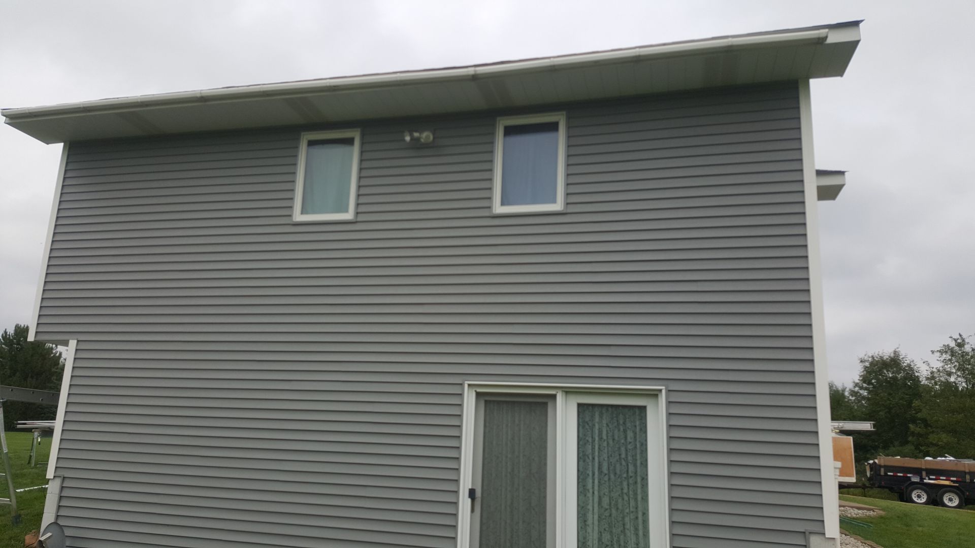 Gray two-story house exterior with vinyl siding, two small upper windows, and a sliding glass door below