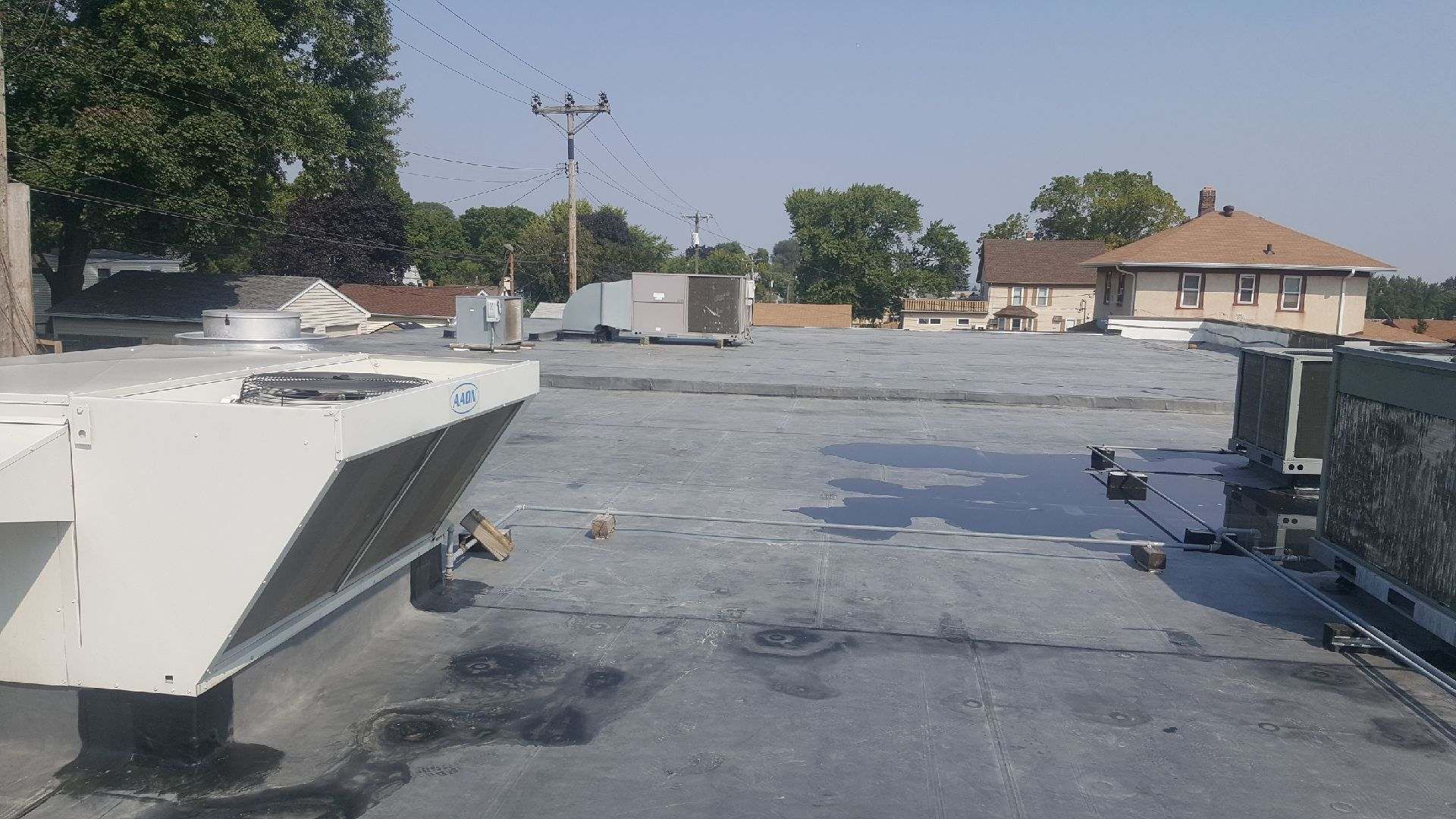 Flat rooftop with HVAC units and vents under a clear sky, with neighboring houses in the distance