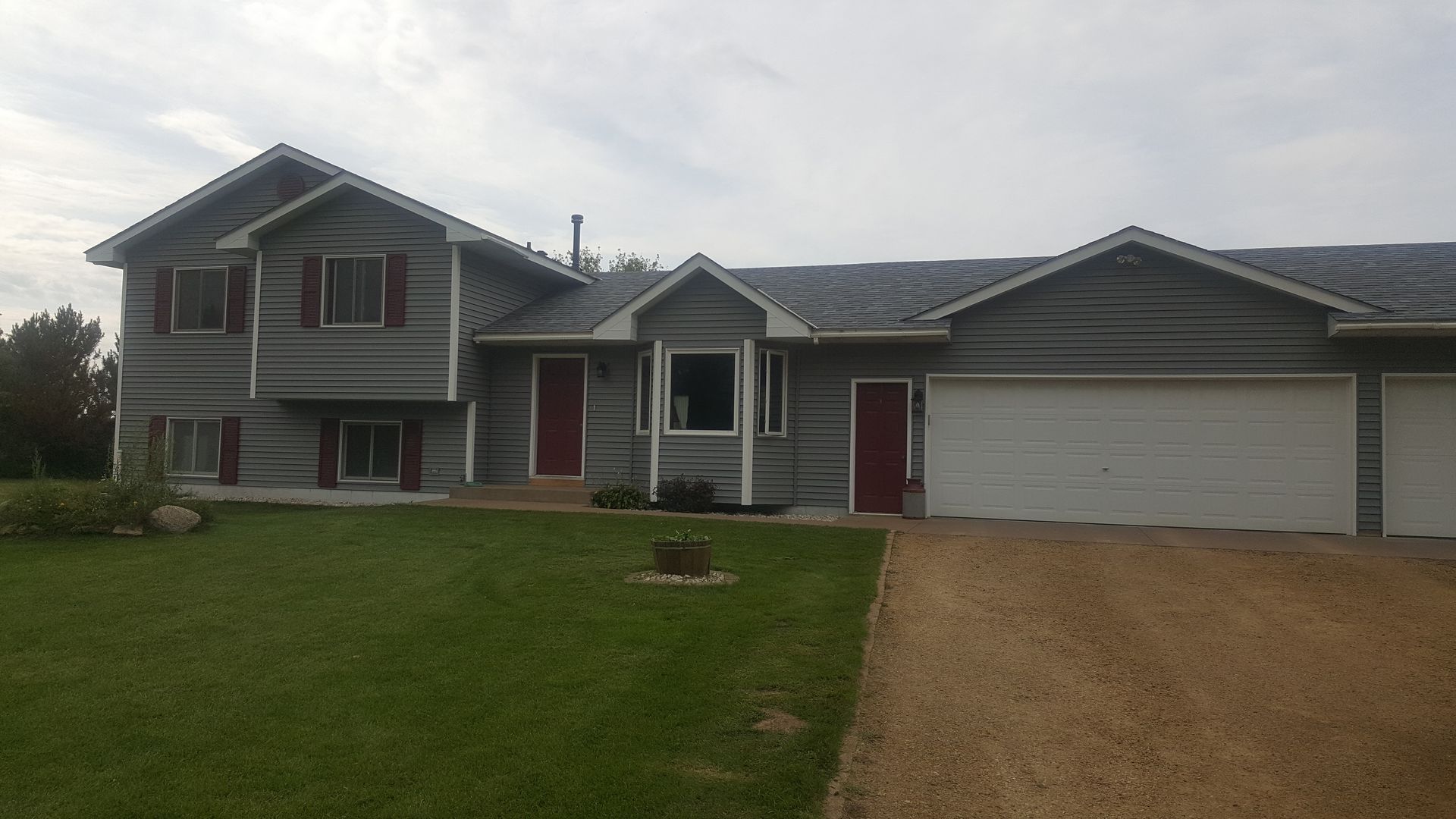 Two-story gray house with red doors, white garage, and a green lawn under a cloudy sky.