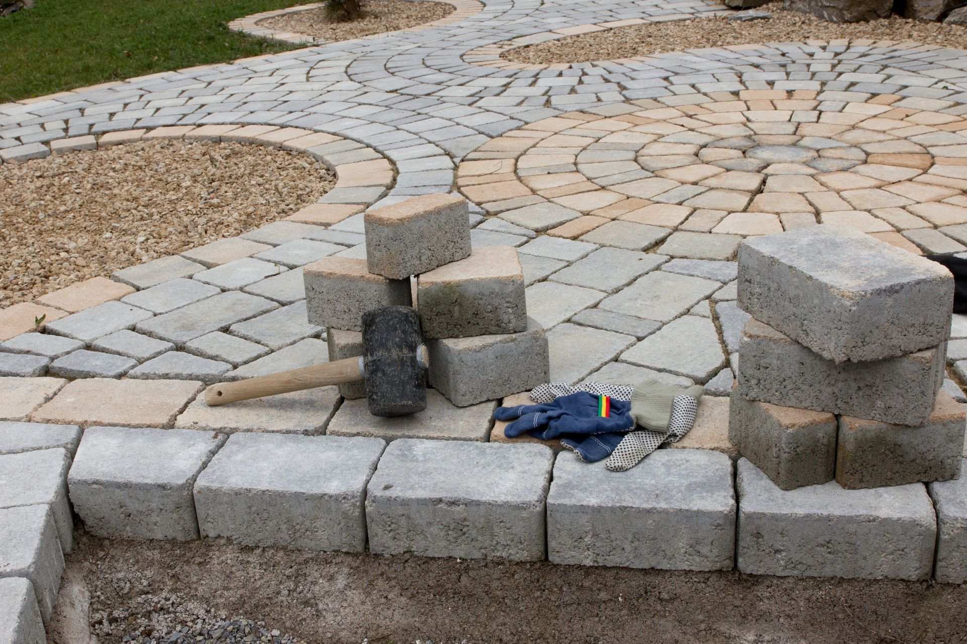 Stone patio under construction with stacked pavers, tools, and curved walkway sections