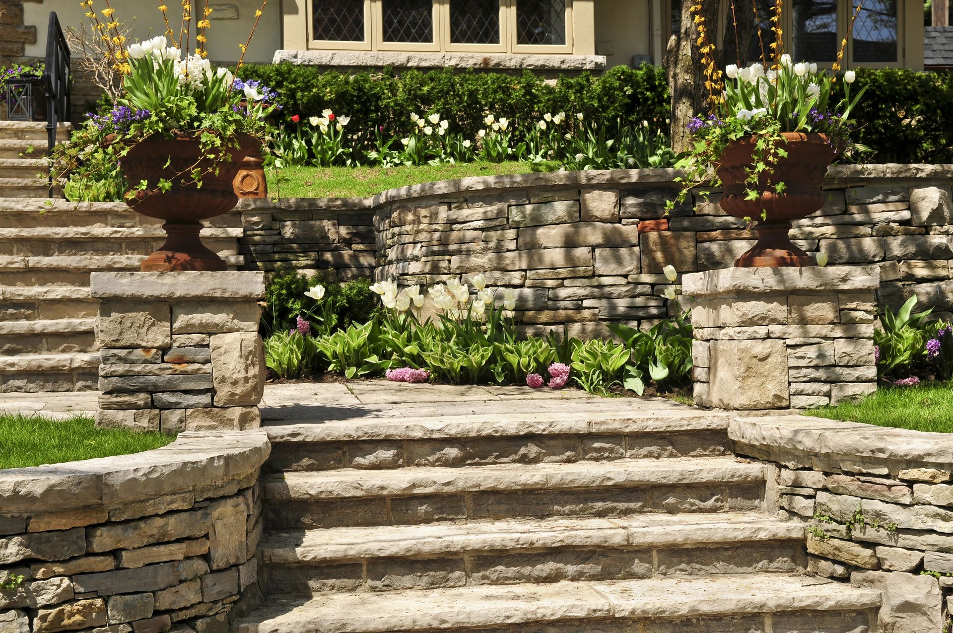 Stone steps leading to a flowered garden terrace with potted plants and stone retaining walls
