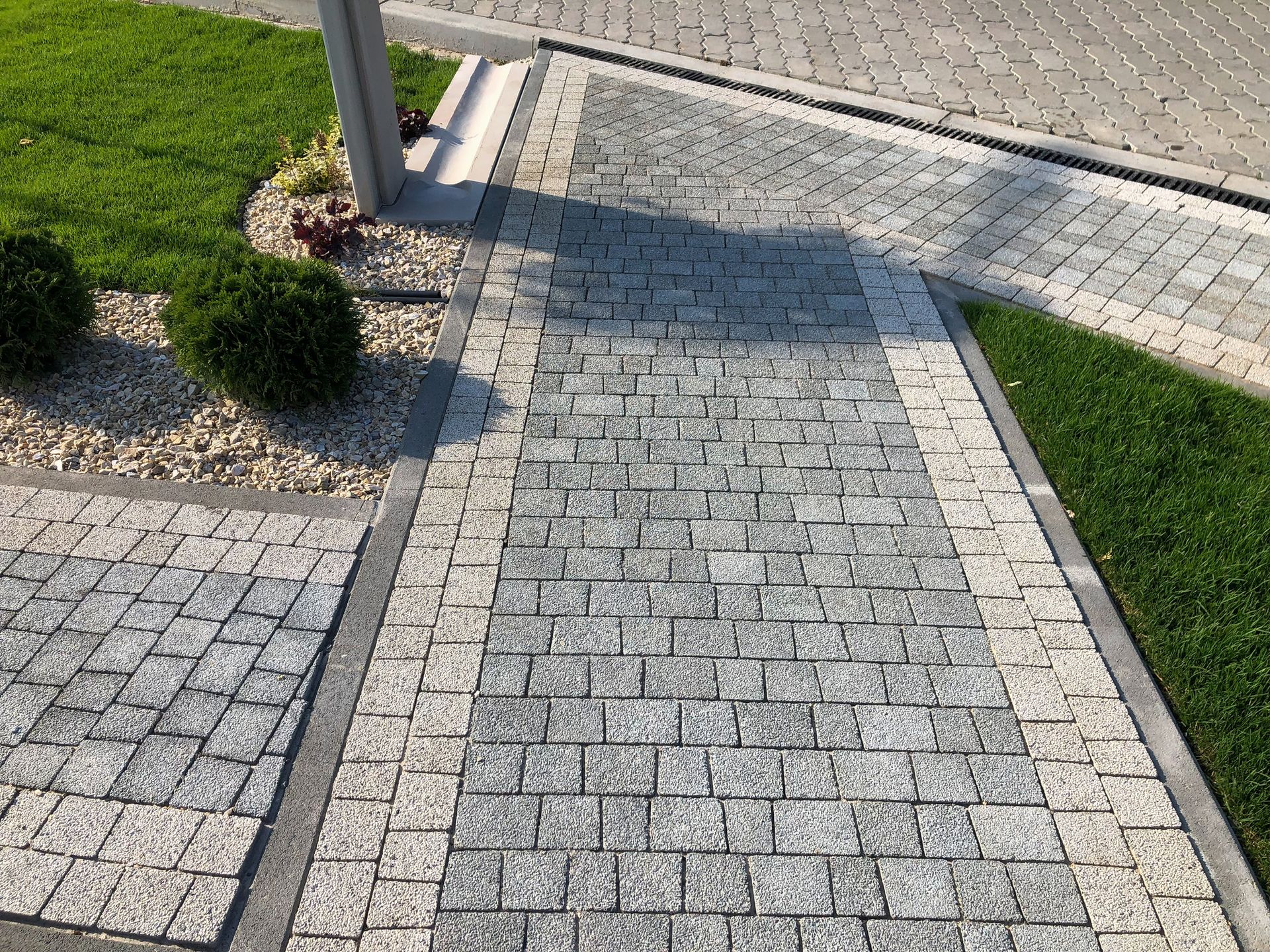 Paved stone walkway curving beside grass and shrubs in bright sunlight