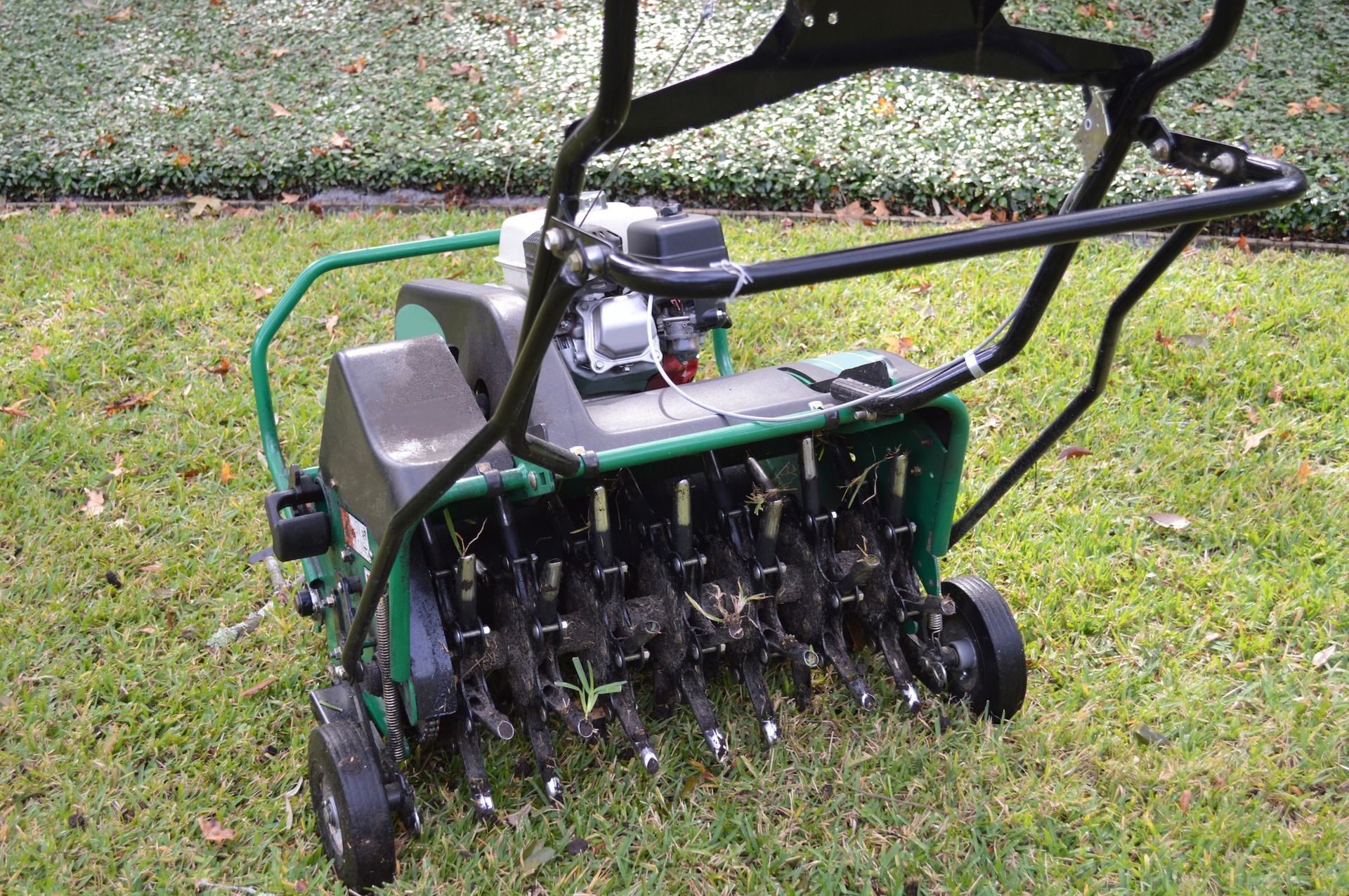 Gas-powered lawn aerator on grass, with black handle and green hose attached.