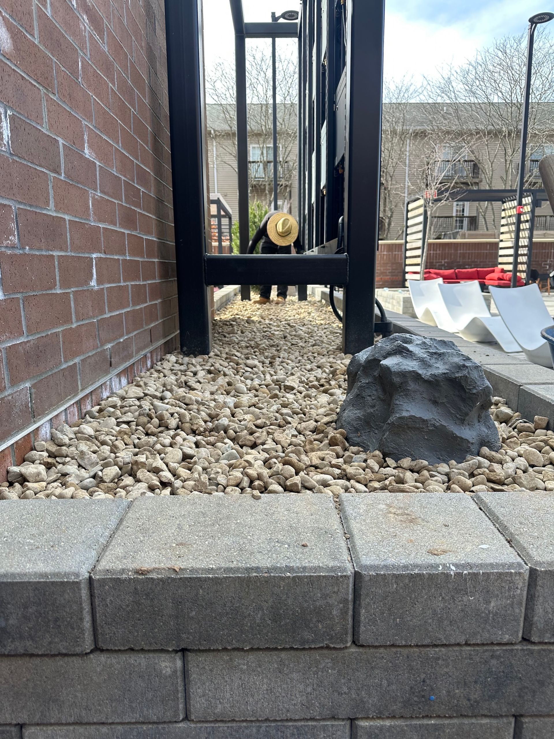 Small outdoor gravel area beside a brick wall, with a black metal structure and a large rock.