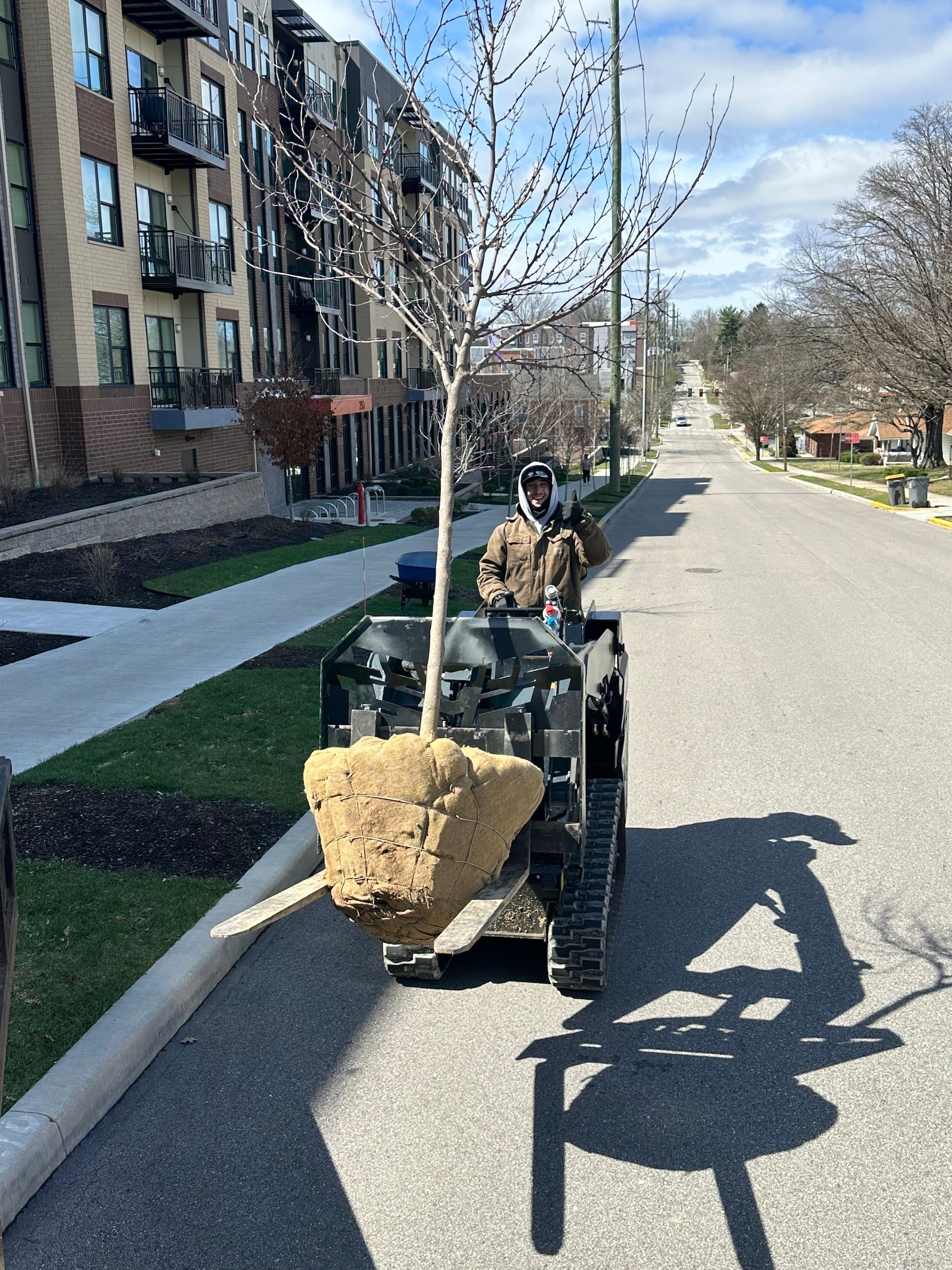 Small loader carrying a large rock on a residential street beside apartment buildings