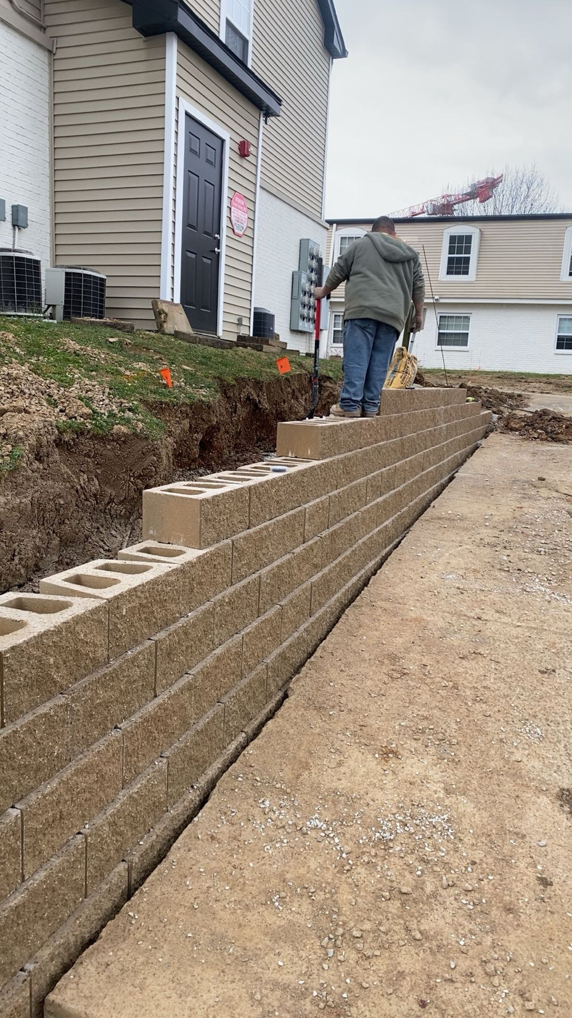 Worker laying a tan retaining wall along a sloped path beside a house