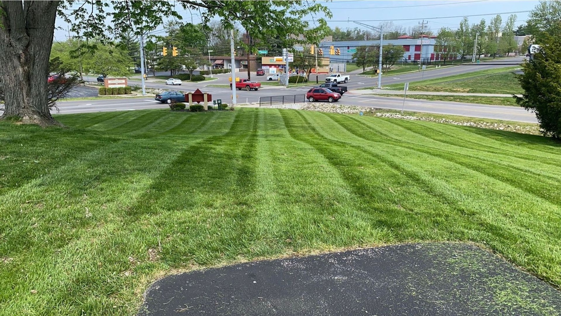 Grassy roadside with striped mowing lines, parked cars, and a gas station in the background