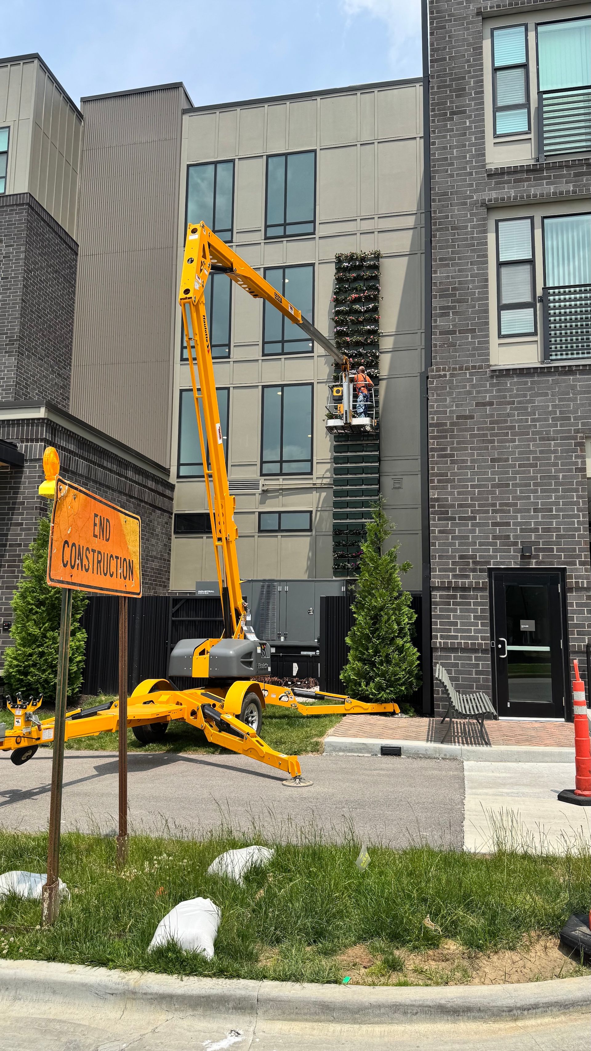 Yellow construction lift beside modern townhouse facade on a sunny street.