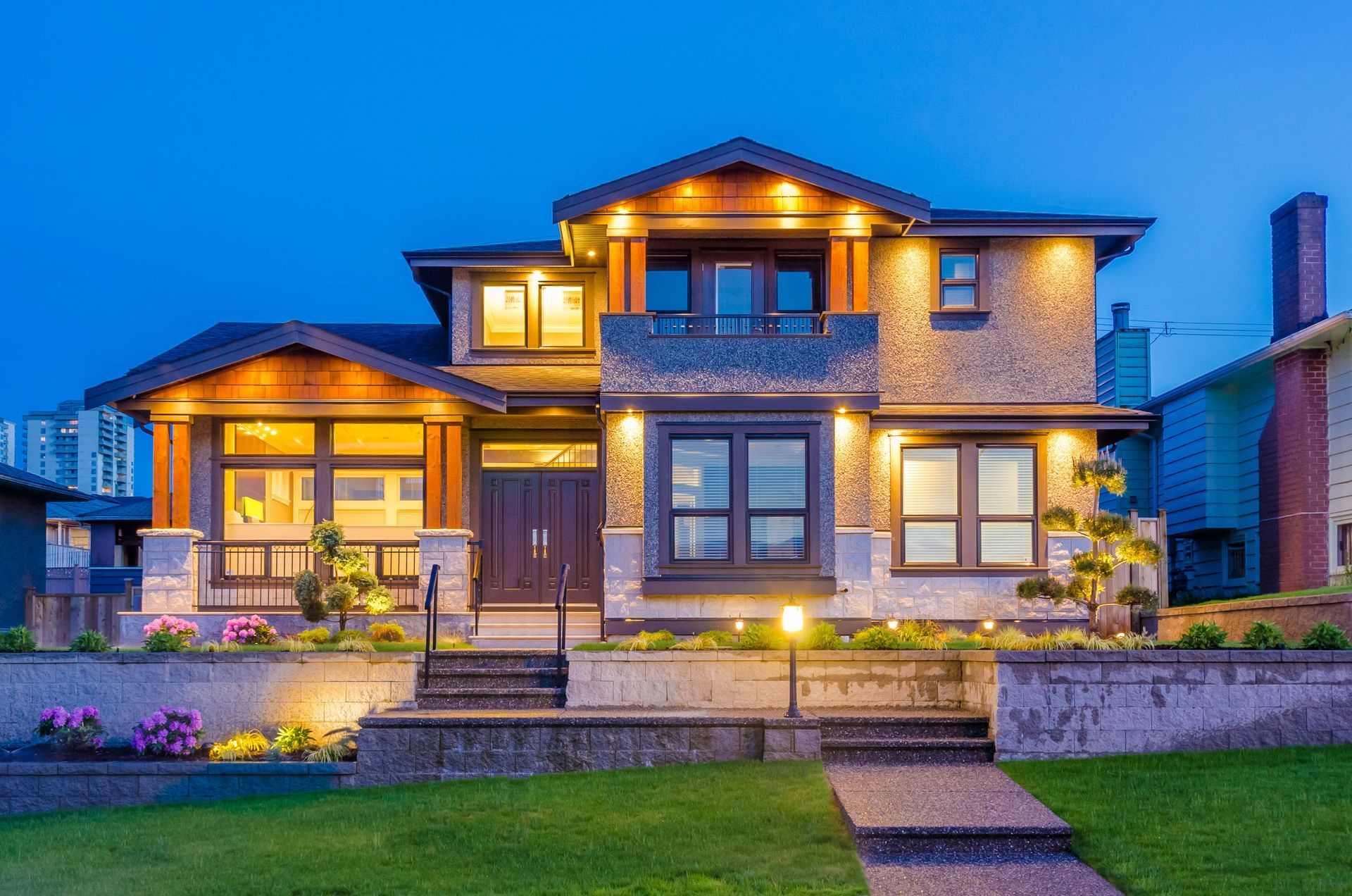 Illuminated modern two-story house with stone facade and landscaped front yard at dusk