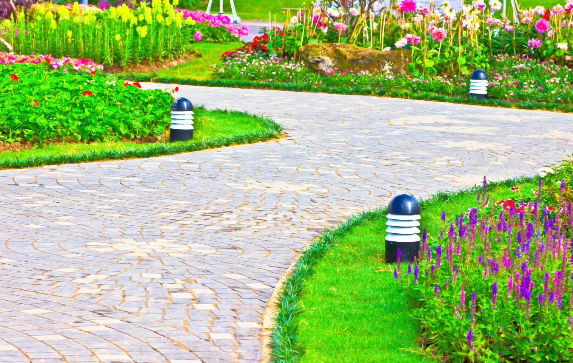 Curving garden path lined with colorful flowers and black-and-white pathway lights
