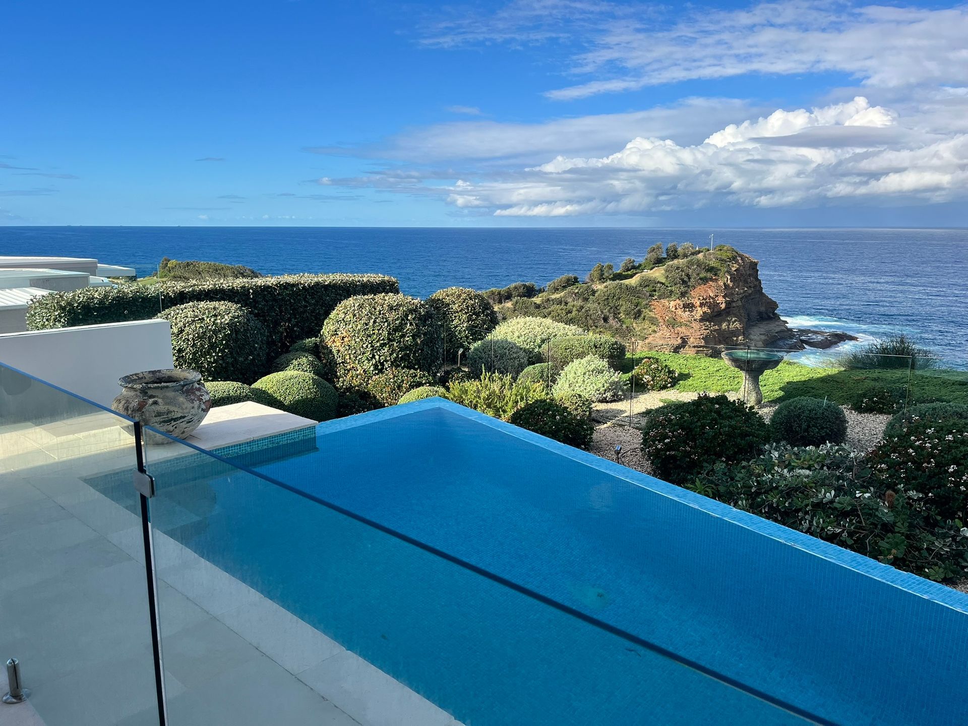 Oceanfront pool with blue water overlooking the sea and rocky coastline under a partly cloudy sky — Divine Landscape Creations in Berkeley Vale, NSW