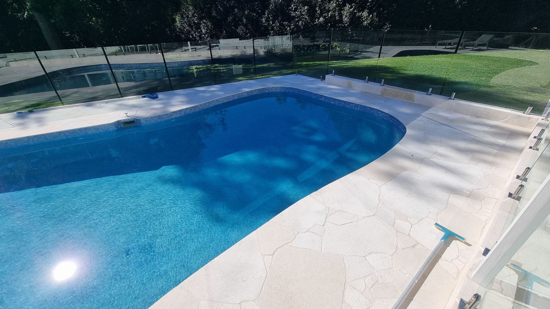 Blue backyard swimming pool beside a white patio in bright sunlight — Divine Landscape Creations in Berkeley Vale, NSW