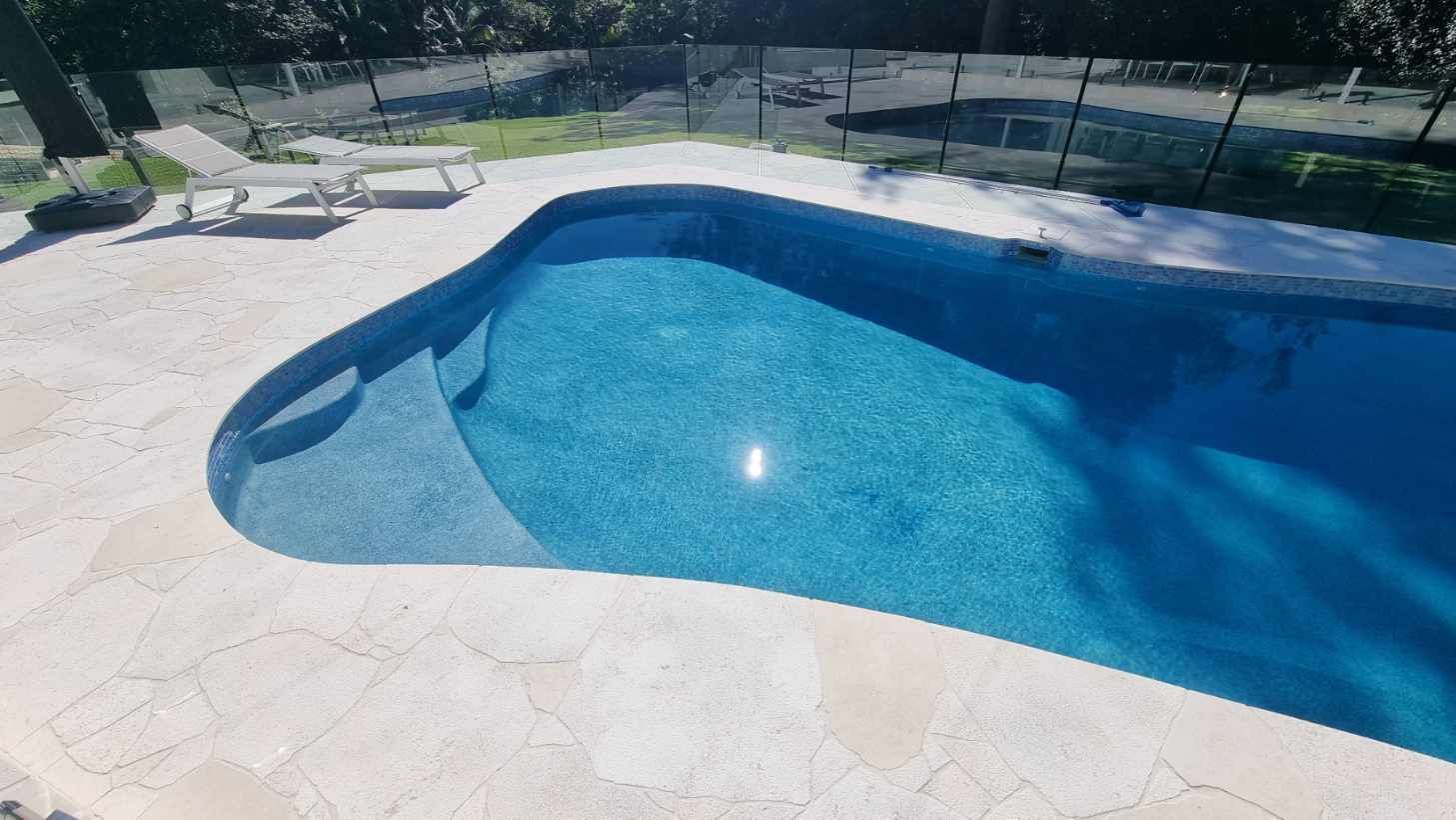 Blue swimming pool with stone deck and lounge chairs in bright sunlight — Divine Landscape Creations in Berkeley Vale, NSW