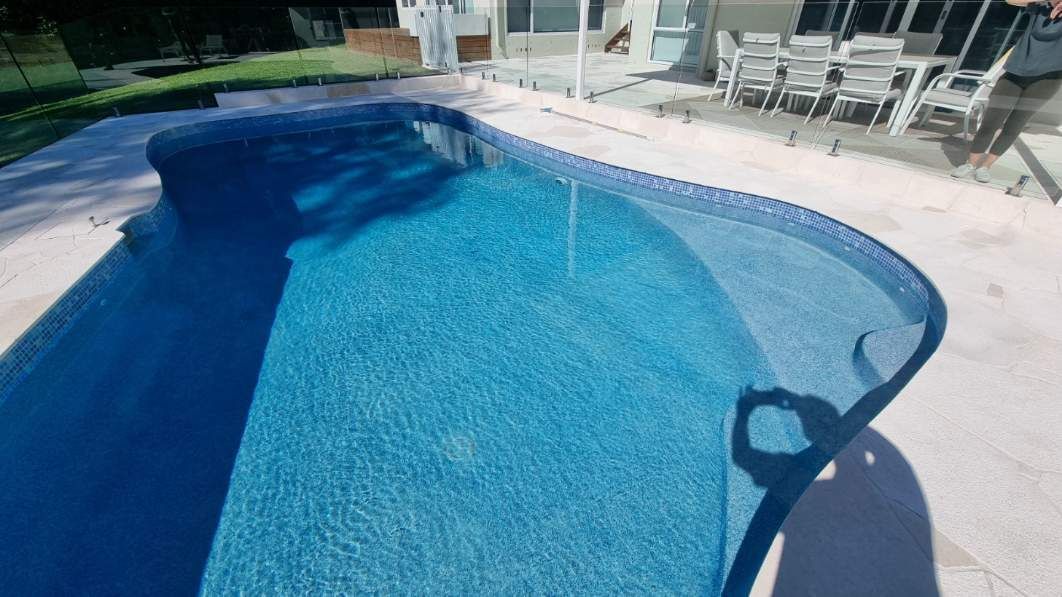 Blue swimming pool with lounge chairs and patio furniture in the background — Divine Landscape Creations in Berkeley Vale, NSW