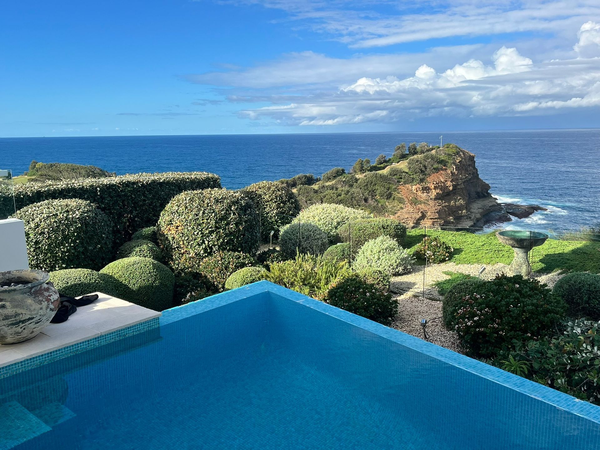 Oceanfront pool with blue water and lush greenery overlooking the sea under a partly cloudy sky — Divine Landscape Creations in Berkeley Vale, NSW